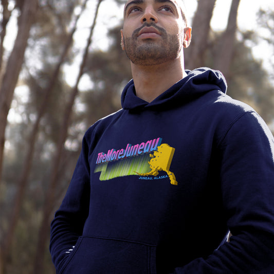 Man wearing a navy blue hoodie with colorful Juneau, Alaska The More Juneau graphic design featuring northern lights, big dipper, and the Last Frontier.