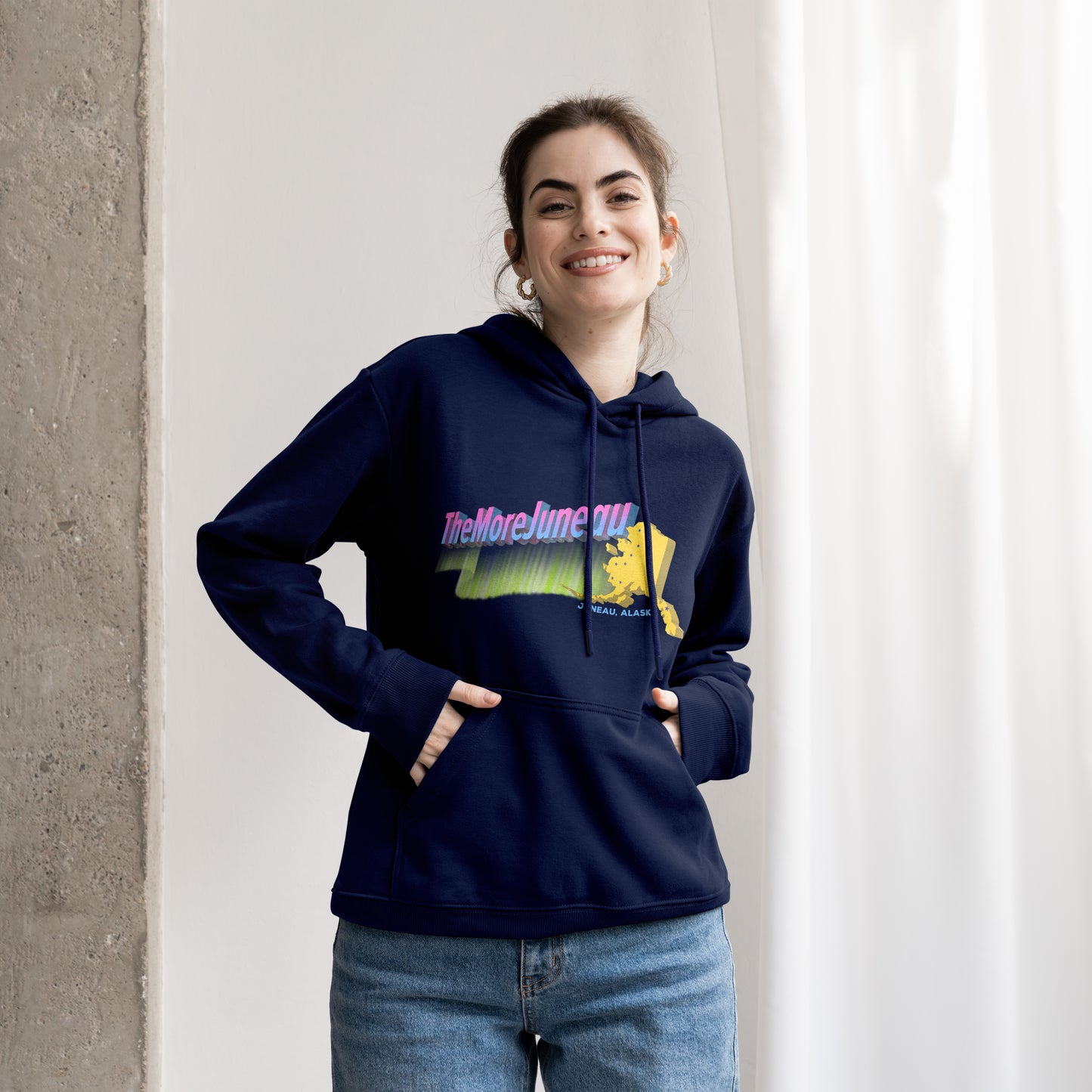 Person wearing a navy blue hoodie with colorful Juneau, Alaska The More Juneau graphic design featuring northern lights, big dipper, and the Last Frontier.